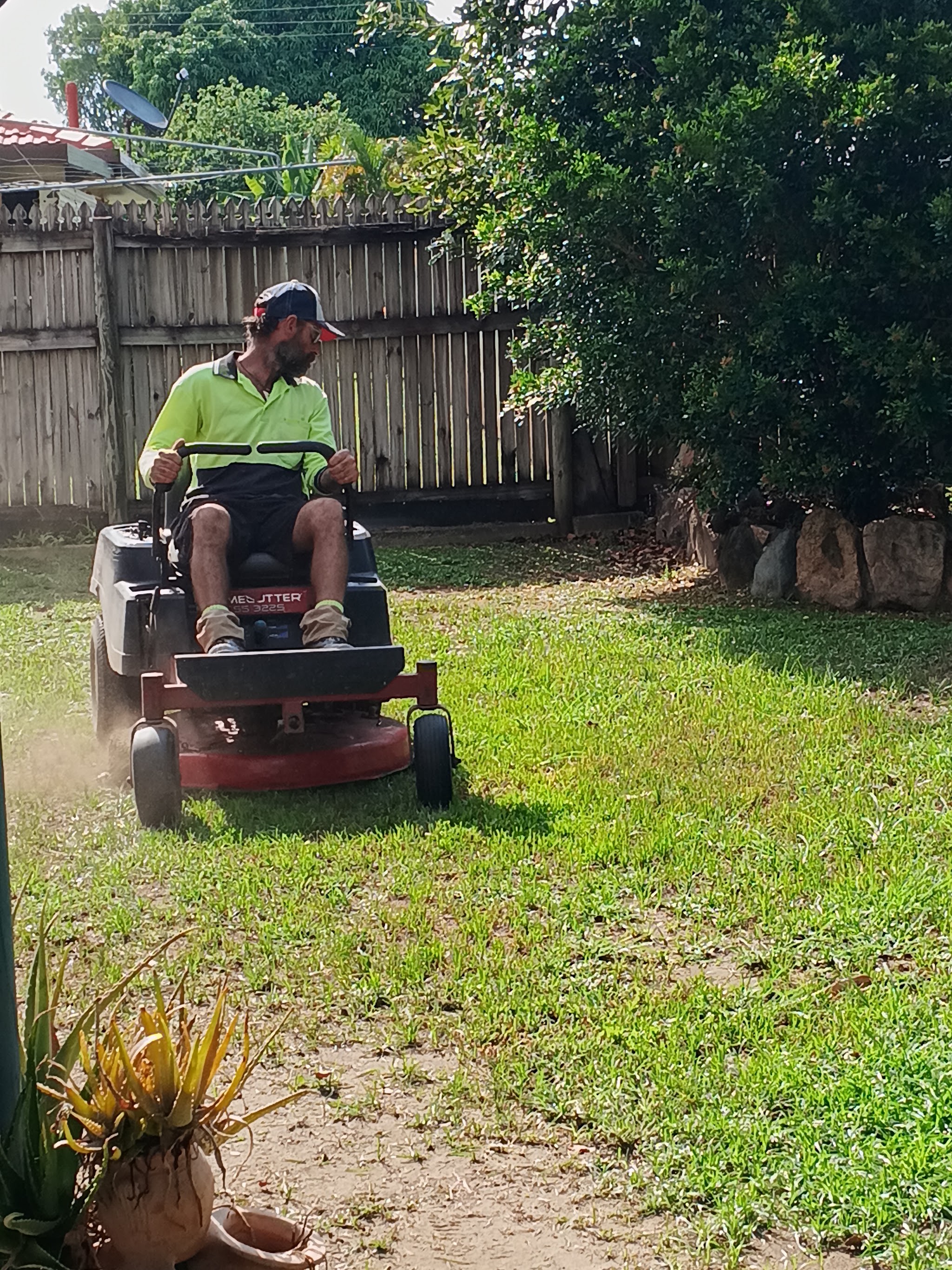 Yanzy's Lawn care mowing a backyard lawn in Townsville on a ride-on mower